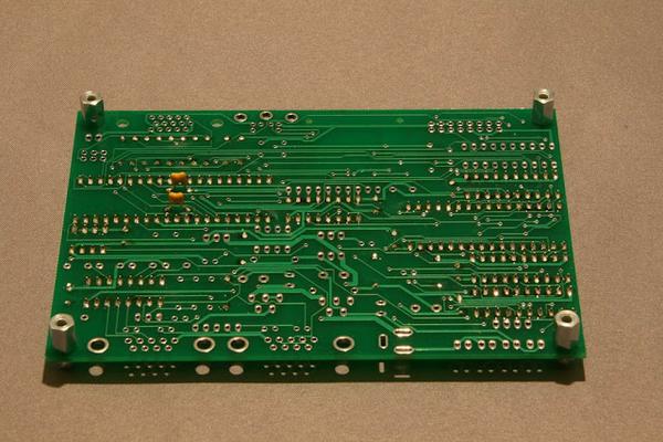 A PCB from solder side with two capacitors mounted.