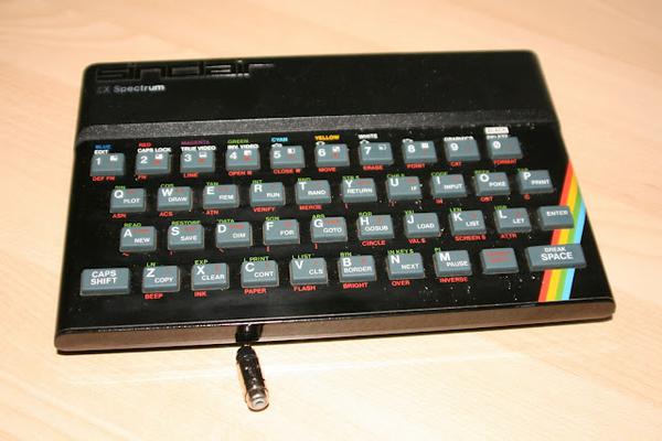 A Sinclair ZX Spectrum with some signs of wear and a phono in line connector infront of it.